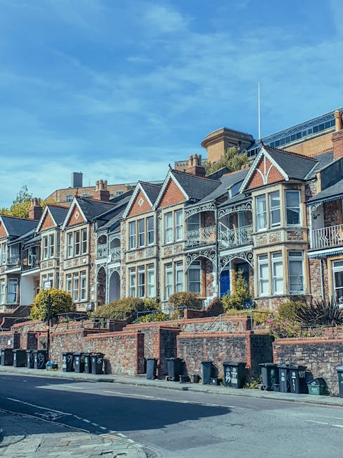 A row of Victorian-style terraced houses situated along a residential street, featuring decorative ironwork on the balconies and detailed brickwork on the facades. The houses are set on a raised platf